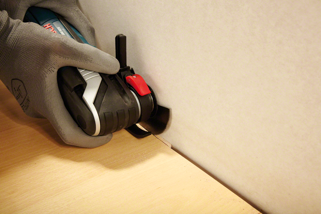 안전 장비를 착용한 사람이 전동 공구를 이용해 벽 가장자리의 나무를 자르고 있습니다.