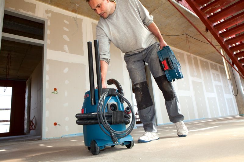 작업복을 입은 사람이 건설 현장에서 전선이 달린 집진기를 옮기고 있습니다.