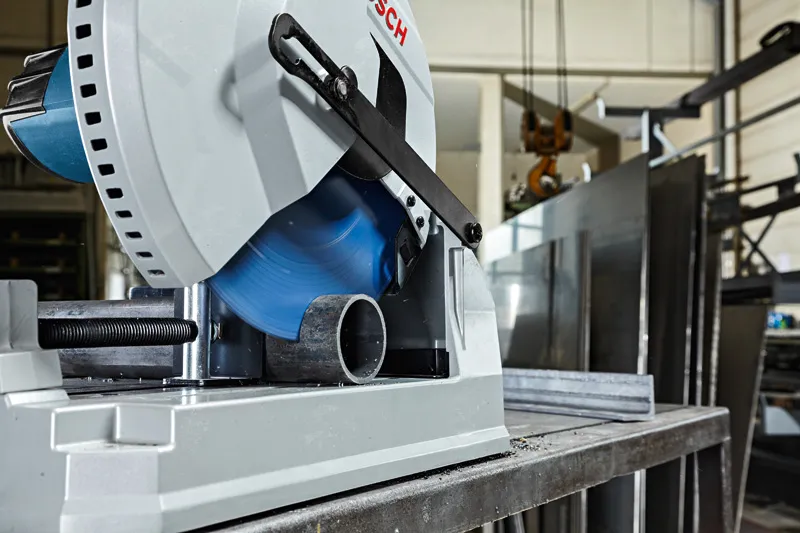 산업 작업장에서 둥근 금속 파이프를 절단하는 금속 절단 톱입니다.