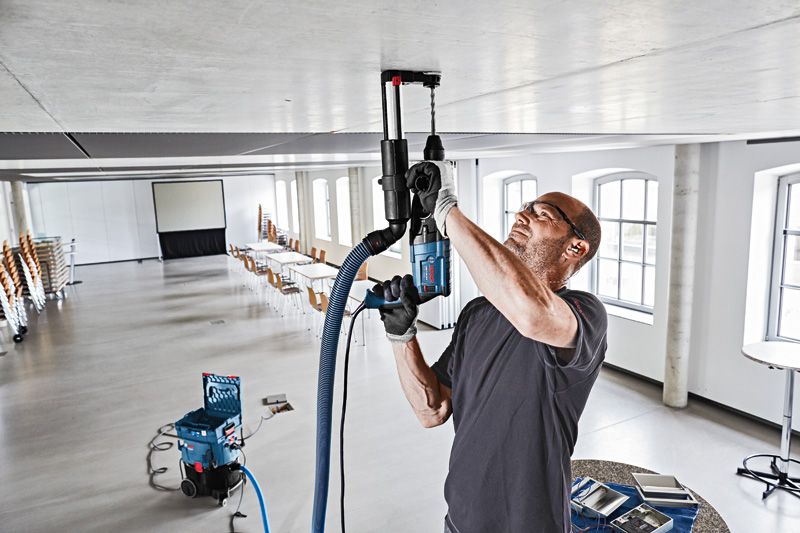 안전장비를 착용한 사람이 먼지 배출 시스템으로 천장에 구멍을 뚫고 있습니다.