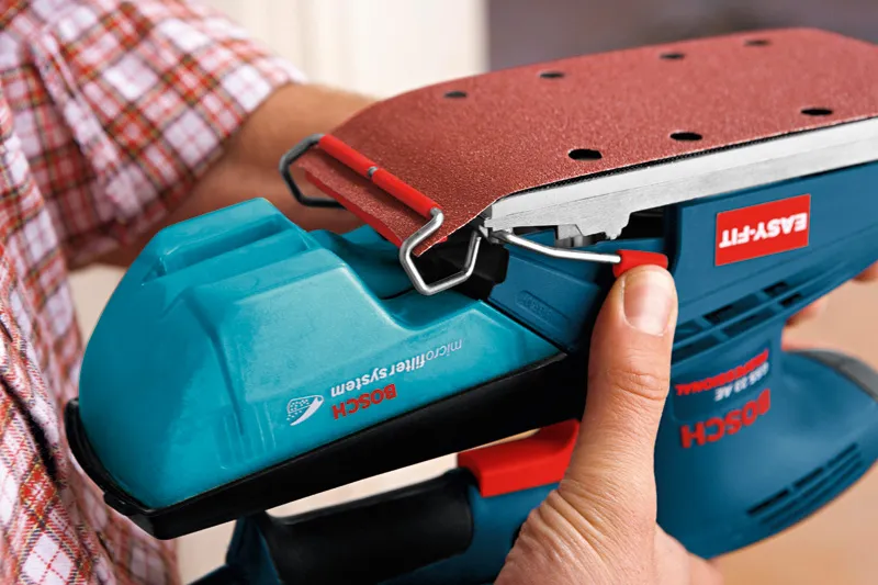 사람이 궤도 샌더에 사포를 부착하고 있습니다.