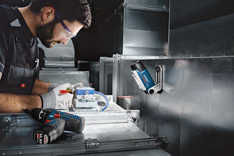 안전 장비를 착용한 사람이 무선 작업등 아래에서 전기 배선 작업을 하고 있습니다.