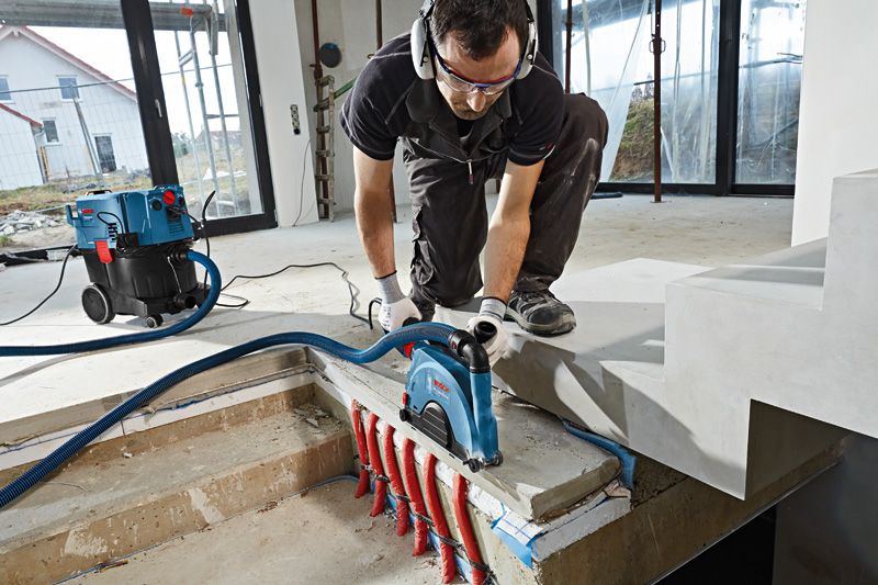 안전 장비를 착용한 사람이 노출된 파이프 위의 콘크리트에 벽 체이서를 사용하고 있습니다.