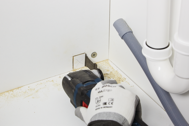 안전 장비를 착용한 작업자가 전동 공구를 이용해 캐비닛에 정사각형 구멍을 자릅니다.