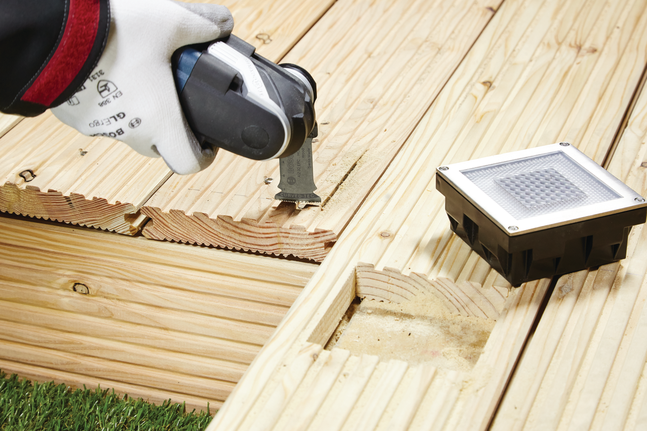 안전 장비를 착용한 작업자가 멀티툴을 이용해 나무 갑판에 홈을 파고 있습니다.