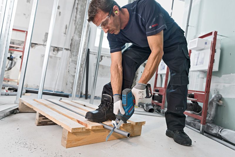 안전 장비를 착용한 사람이 왕복톱을 사용해 금속 파이프를 자릅니다.