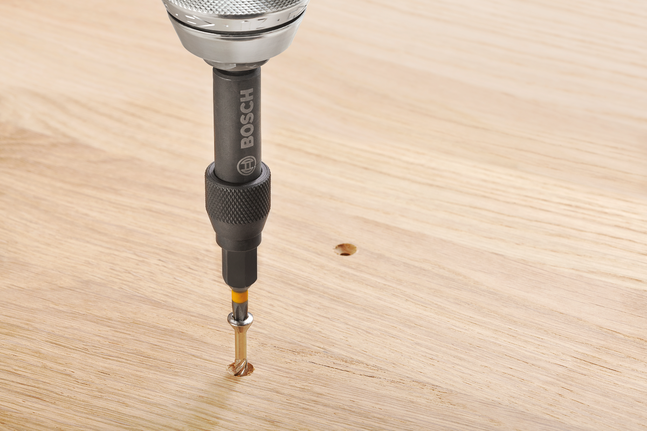 드릴 드라이버가 나무 표면에 구멍을 뚫고 있습니다.