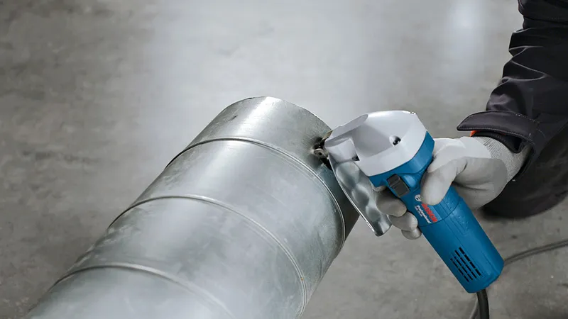 안전 장비를 착용한 사람이 가위를 사용하여 금속 환기 덕트를 절단하고 있습니다.