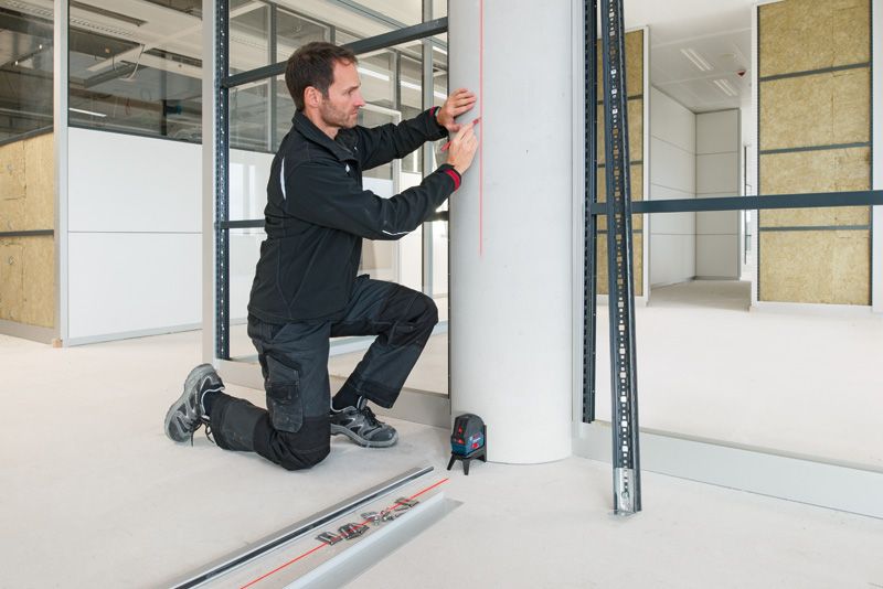 작업복을 입은 사람이 레이저 레벨링 도구를 사용하여 기둥에 표시를 하고 있습니다.