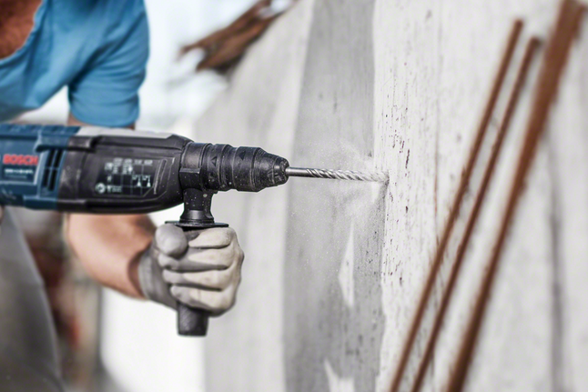 안전장비를 착용한 사람이 콘크리트 벽에 구멍을 뚫고 있습니다.