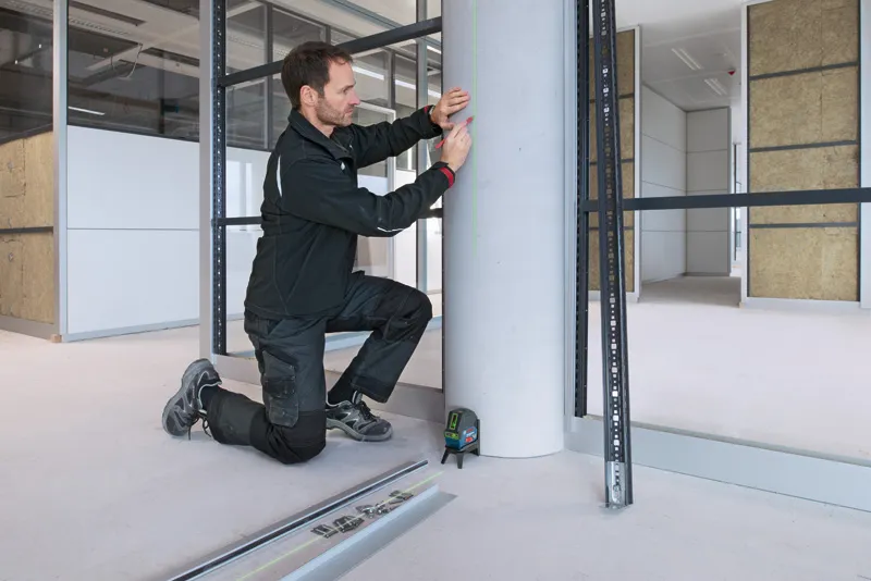 안전장비를 착용한 사람이 레이저 레벨링 도구를 사용하여 콘크리트 기둥에 표시를 하고 있습니다.