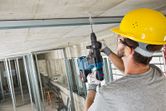 안전장비를 착용한 사람이 공사 중 콘크리트 천장에 구멍을 뚫고 있다.