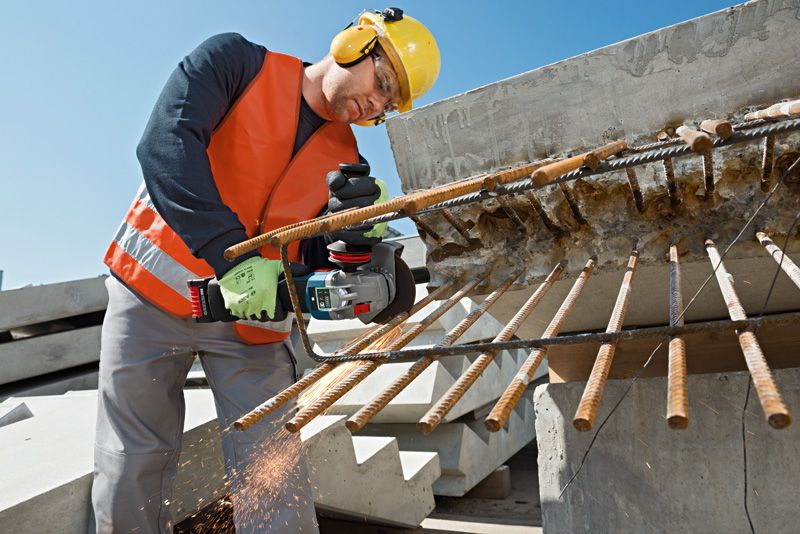 안전 장비를 착용한 사람이 건설 현장에서 전동 공구를 이용해 튀어나온 철근을 자르고 있습니다.