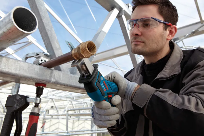 GSA 10.8V-Li 안전 장비를 착용한 사람이 무선 왕복톱을 사용하여 금속 파이프를 절단하고 있습니다.