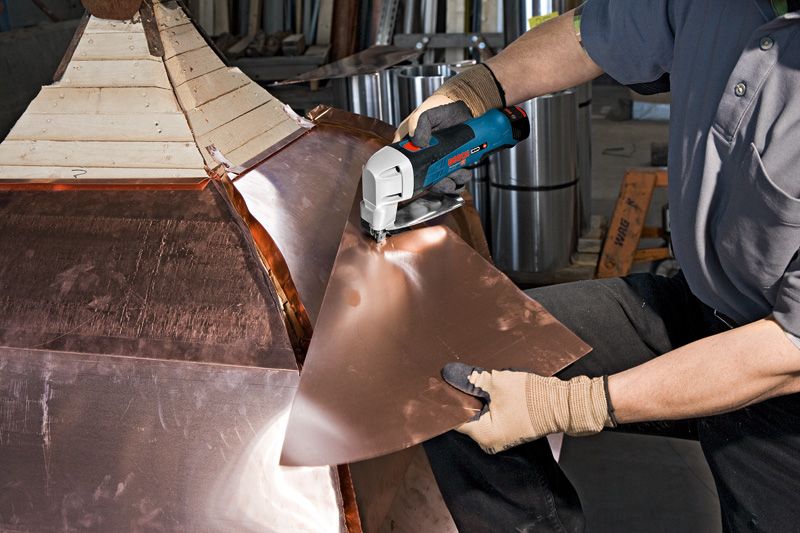 GSC 12V-13 안전 장비를 착용한 사람이 무선 금속 가위로 금속판을 자르고 있습니다.