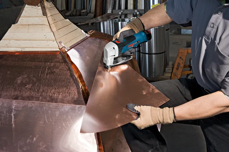 안전 장비를 착용한 사람이 무선 금속 가위로 금속판을 자르고 있습니다.