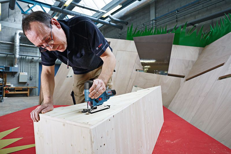 한 사람이 작업장에서 무선 톱을 사용해 나무를 자르고 있다.