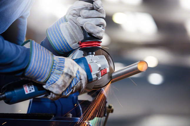 안전 장비를 착용한 작업자가 각도 그라인더로 금속 파이프를 갈고 있습니다.