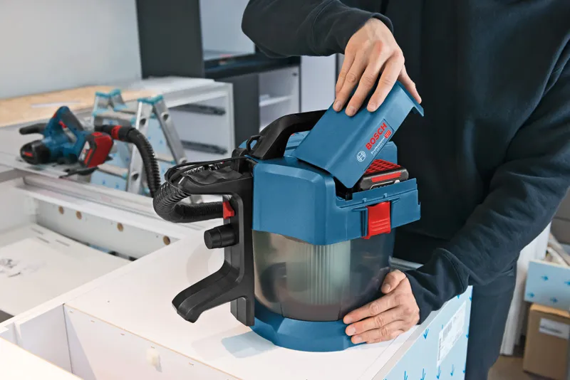 사람이 작업대 위에 있는 무선 집진기에 배터리를 넣고 있습니다.