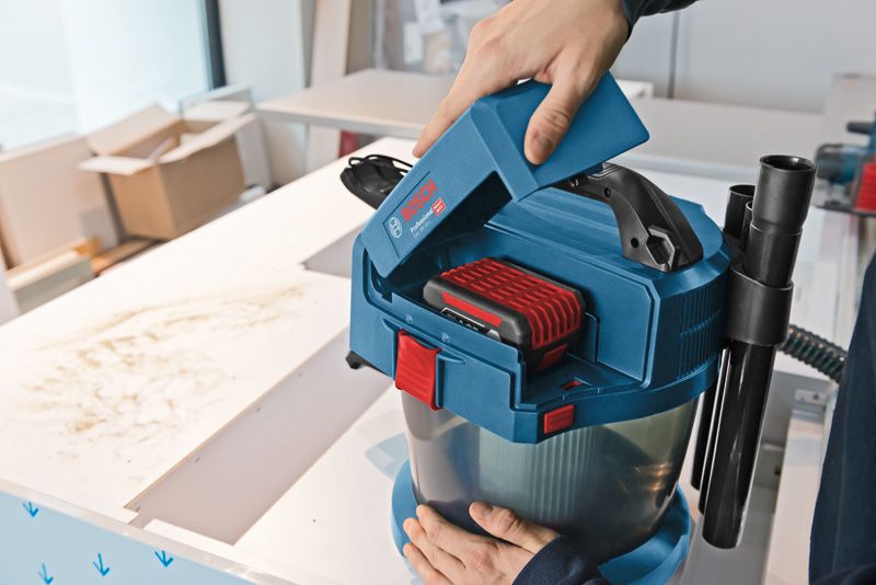 GAS 18V-10 L 한 사람이 작업대 위에 있는 무선 집진기에 배터리를 넣고 있습니다.