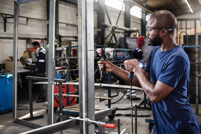 HSS 트위스트 드릴 비트 PointTeQ 19피스 ProBox 1 - 10mm 안전 장비를 착용한 사람이 산업 작업장에서 금속 프레임에 드릴을 박고 있습니다.