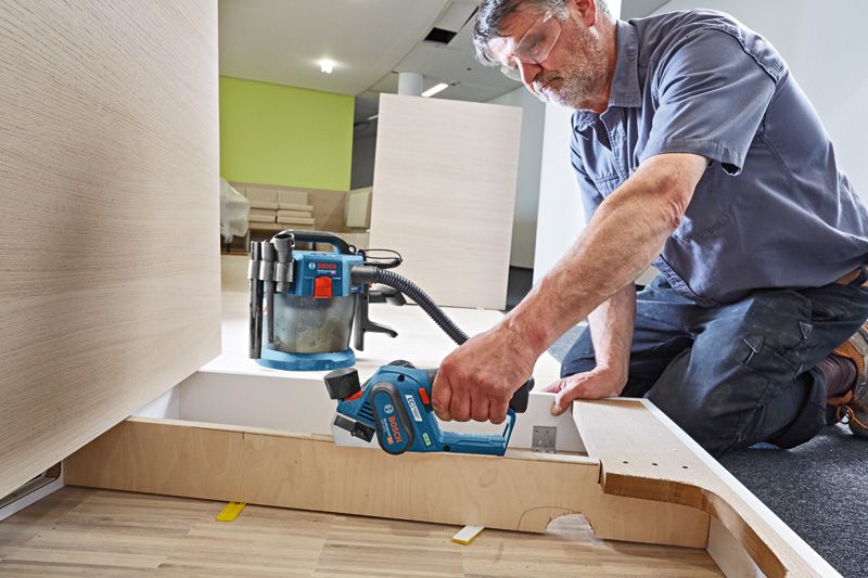 안전 장비를 착용한 사람이 무선 평면기를 사용하여 나무 패널을 매끄럽게 다듬고 있습니다.