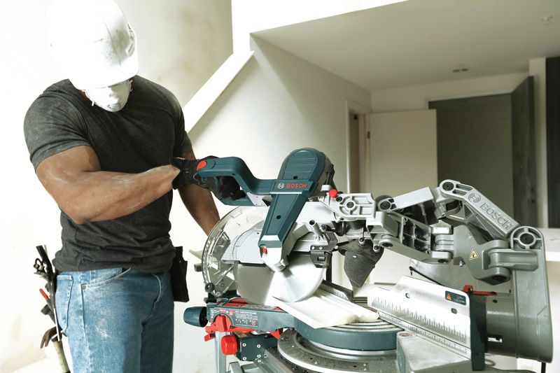 안전 장비를 착용한 사람이 공사 중인 방에서 마이터 톱을 조정하고 있습니다.