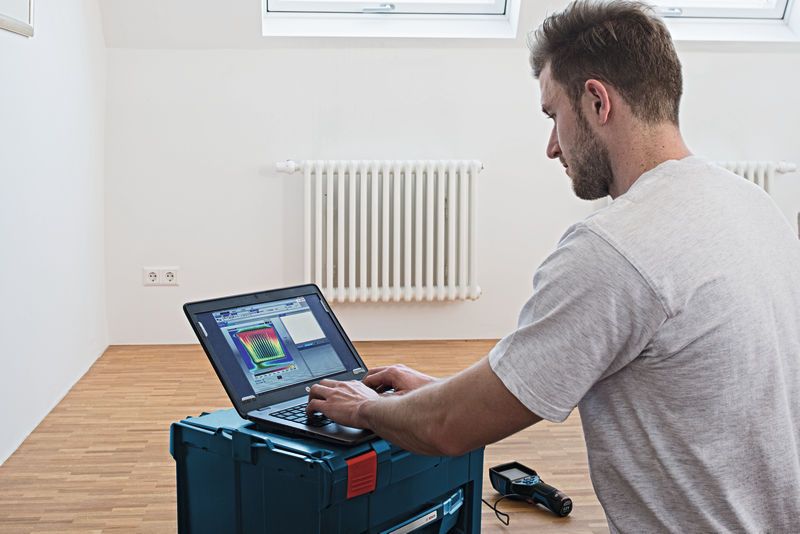 라디에이터가 있는 방에서 노트북으로 열 카메라 데이터를 분석하는 사람.