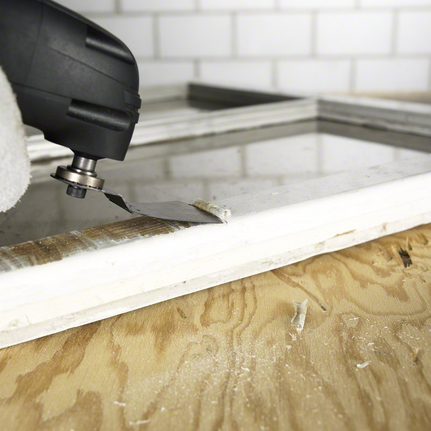 안전 장비를 착용한 사람이 다용도 공구를 사용하여 창틀에서 재료를 제거하고 있습니다.