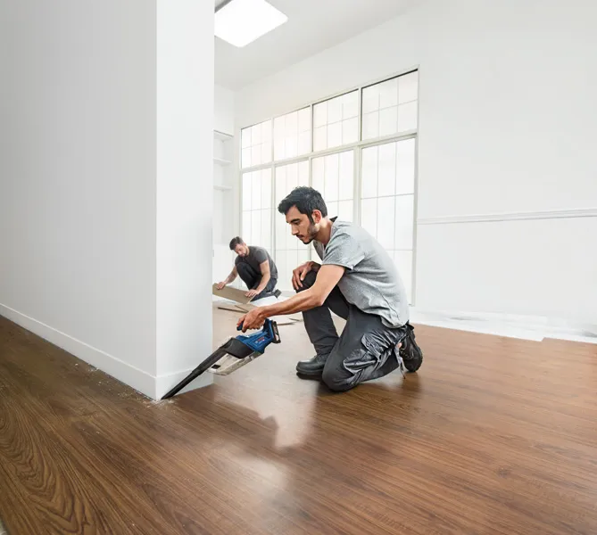 한 사람이 무선 톱을 이용해 벽 근처의 바닥을 자르는 동안 다른 사람은 바닥 패널을 설치합니다.