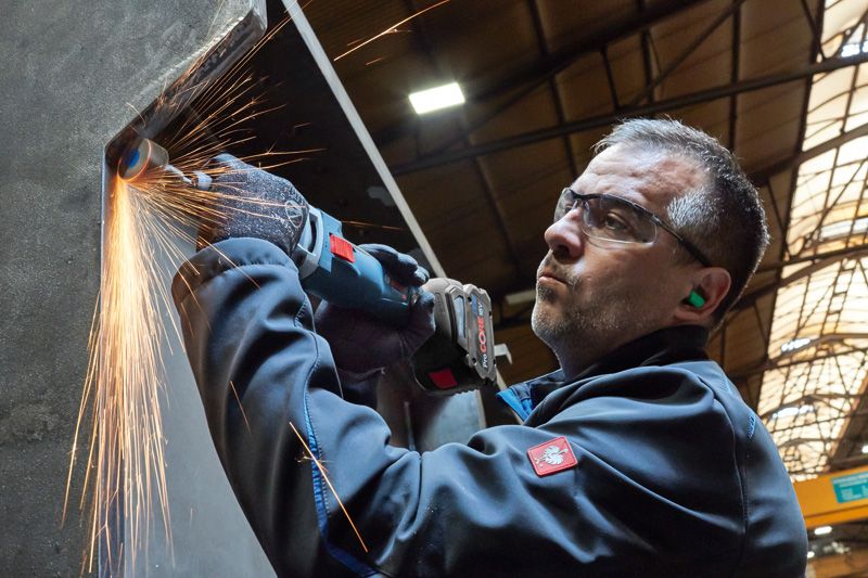 GGS 18V-23 LC 안전장비를 착용한 사람이 금속을 갈아서 밝은 불꽃을 낸다.