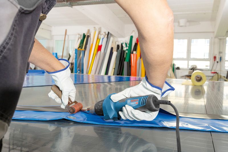 안전장비를 착용한 사람이 열선총을 이용해 플라스틱 시트를 용접하고 있습니다.