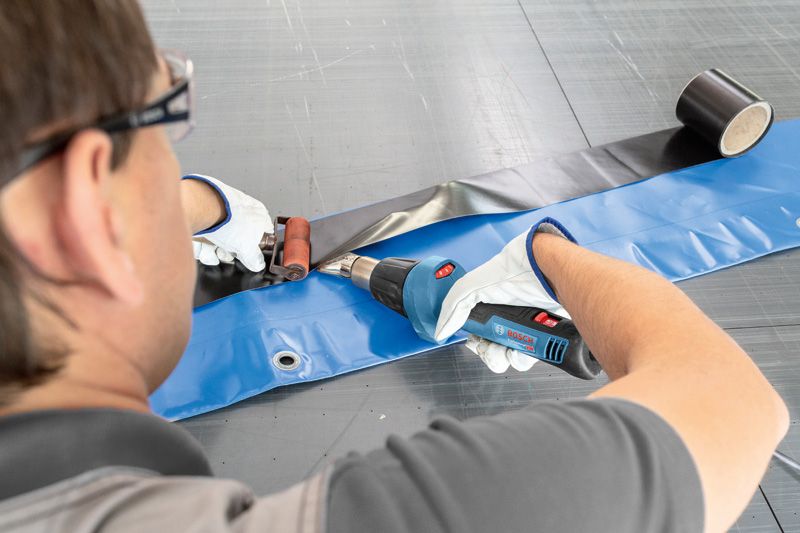 안전 장비를 착용한 사람이 열풍총을 사용해 플라스틱 시트를 밀봉하고 있습니다.