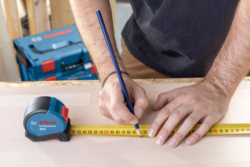 사람이 테이프 측정기를 이용해 연필로 나무에 측정값을 표시하고 있습니다.