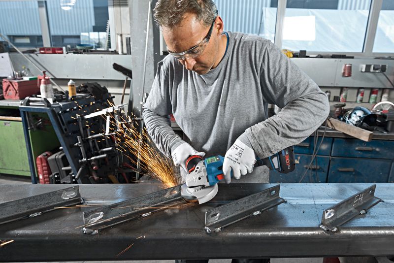 GWS 18V-15 SC 안전 장비를 착용한 사람이 각도 분쇄기를 사용하여 금속 빔을 자릅니다.