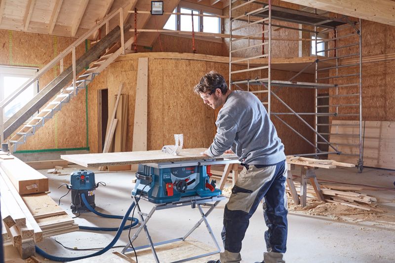 한 사람이 부분적으로 건설된 건물에서 나무를 자르기 위해 원반 톱을 조작하고 있습니다.