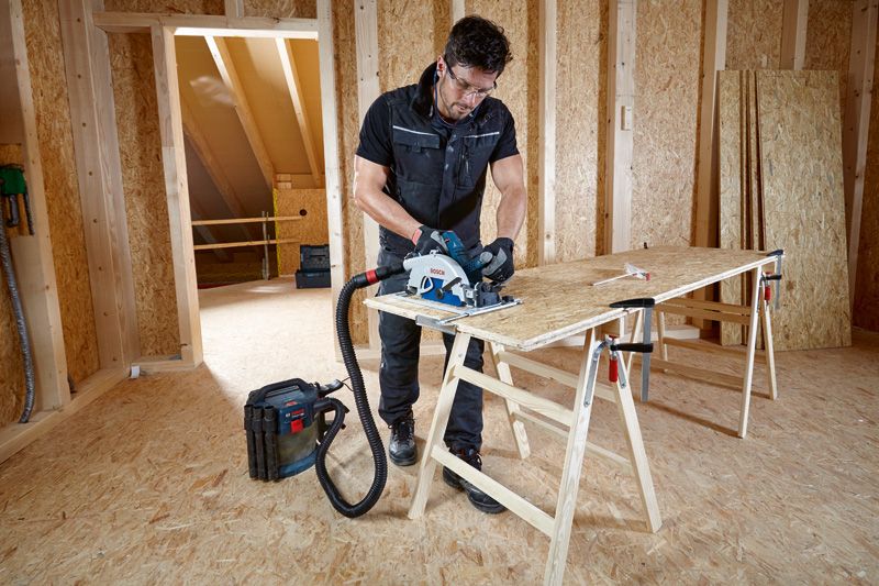 안전 장비를 착용한 사람이 집진기에 연결된 원형 톱을 이용해 합판을 자릅니다.