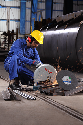 안전 장비를 착용한 사람이 절단톱으로 금속 파이프를 자르면서 불꽃이 튀고 있다.