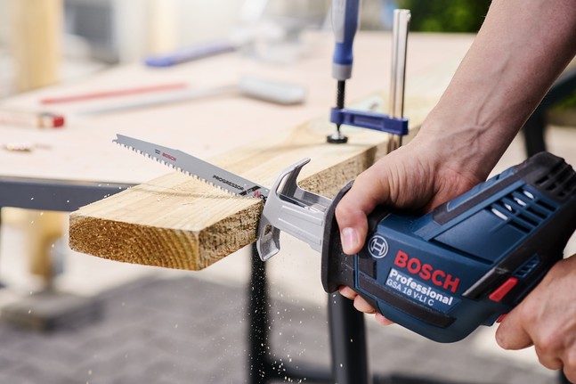 한 사람이 작업대 위에서 왕복톱을 사용하여 나무 판자를 자르고 있습니다.