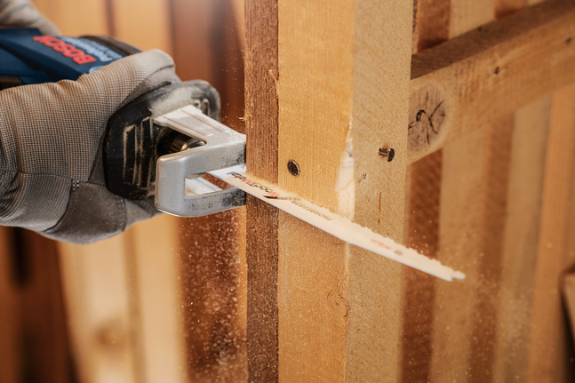 안전 장비를 착용한 사람이 왕복톱으로 나무 기둥을 자르고 있습니다.