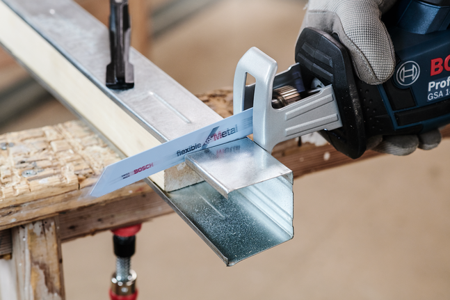 안전 장비를 착용한 사람이 왕복톱을 사용하여 금속 채널을 절단하고 있습니다.