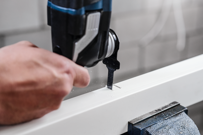 한 사람이 직소톱을 사용하여 흰색 칠판에 직사각형 홈을 파고 있습니다.