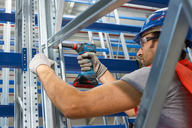 GDX 18V-200 안전 장비를 착용한 사람이 금속 프레임에 무선 드릴을 사용하고 있습니다.