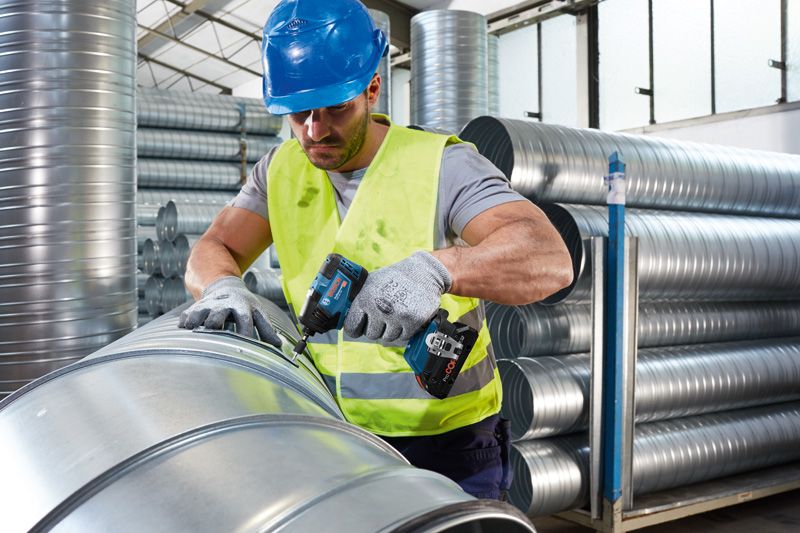 안전 장비를 착용한 사람이 무선 전동 공구를 사용하여 금속 배관을 고정하고 있습니다.