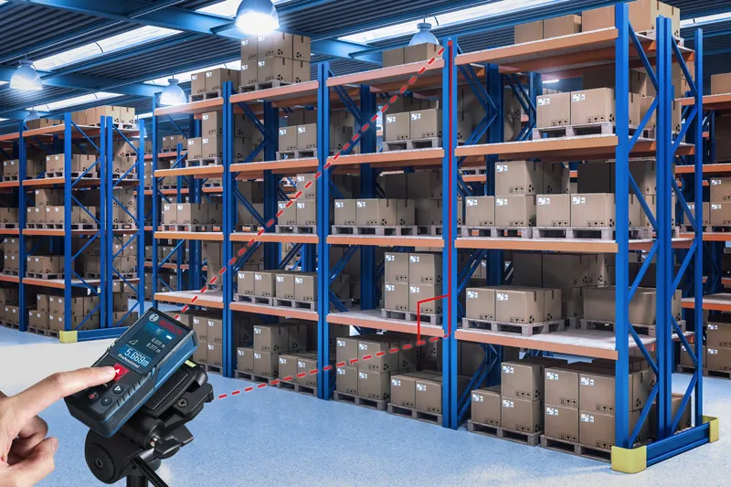 한 사람이 레이저 측정기를 사용해 창고 선반 사이의 거리를 확인하고 있습니다.