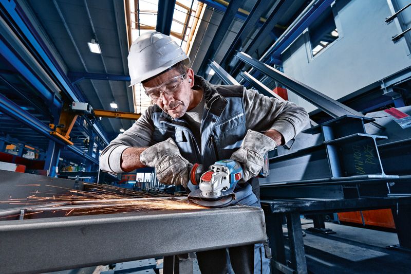 안전 장비를 착용한 사람이 무선 각도 그라인더로 금속을 갈고 있습니다.