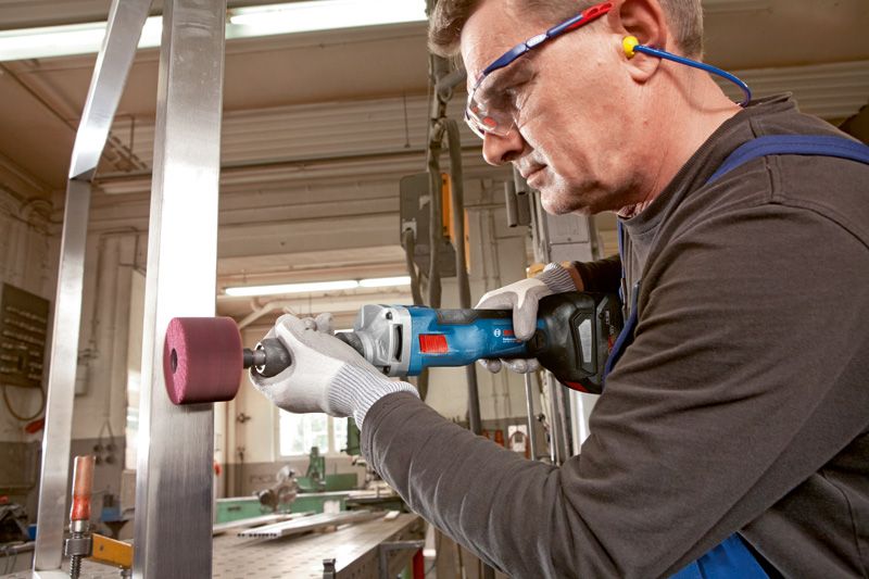 안전 장비를 착용한 사람이 강철 보에 무선 직선 그라인더를 사용하고 있습니다.