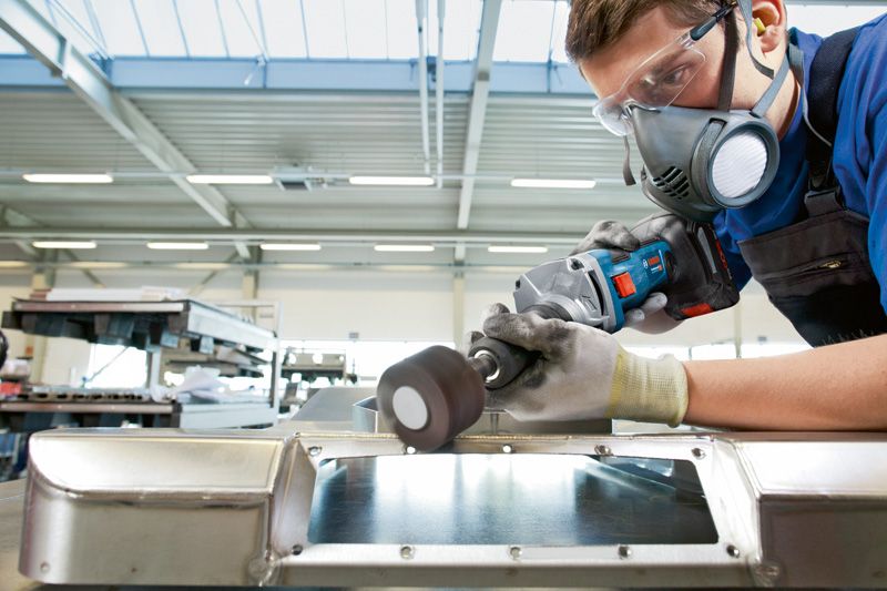 안전 장비를 착용한 사람이 무선 스트레이트 그라인더로 금속 표면을 갈고 있습니다.