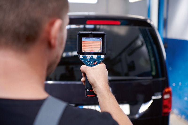 사람이 열화상 카메라를 이용해 차량의 뒷창을 스캔합니다.