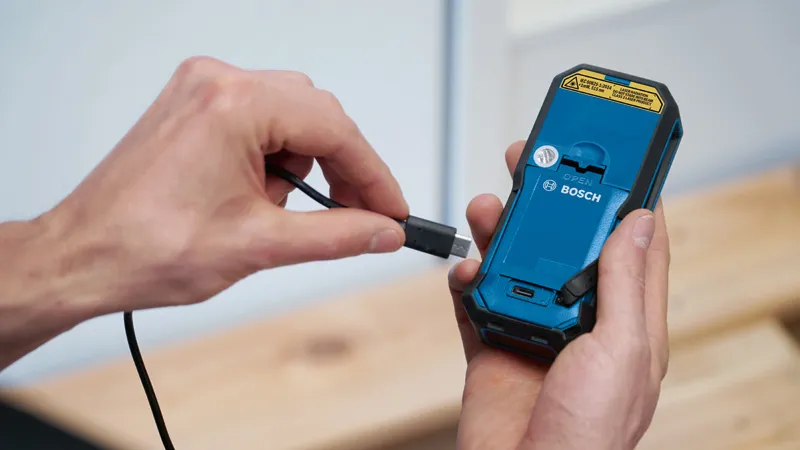 한 사람이 휴대용 전동 공구의 뒷면에 충전 케이블을 연결합니다.